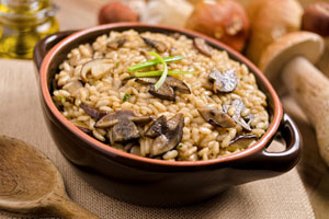 A small brown bowl is full of a hearty rice and mushrooms side dish, surrounded by whole mushrooms in the background.