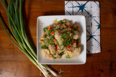An overhead image of a square white plate of homemade, diabetic-friendly chicken fried rice. The plate sits next to a bunch of green onions and a white and blue patterned napkin.