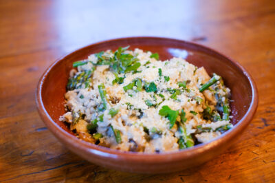 A brown bowl full of mushroom asparagus risotto made with It’s Skinny rice and garnished with leafy green asparagus tops.