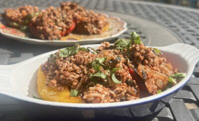 A close-up of two dishes of diabetic-friendly stuffed bell peppers. Yellow peppers are filled with a meat and rice mixture with tomato sauce, spices, and a fresh herb garnish.