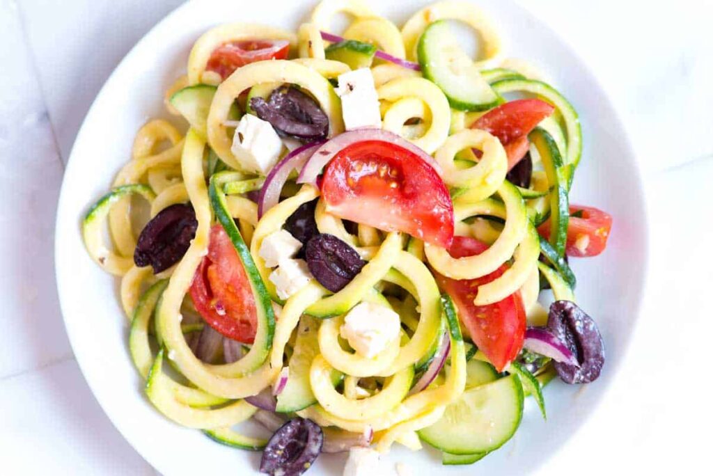 Squiggles of tasty cooked zucchini noodles are mixed with fresh tomatoes, olives, and feta cheese for a low-carb pasta salad.