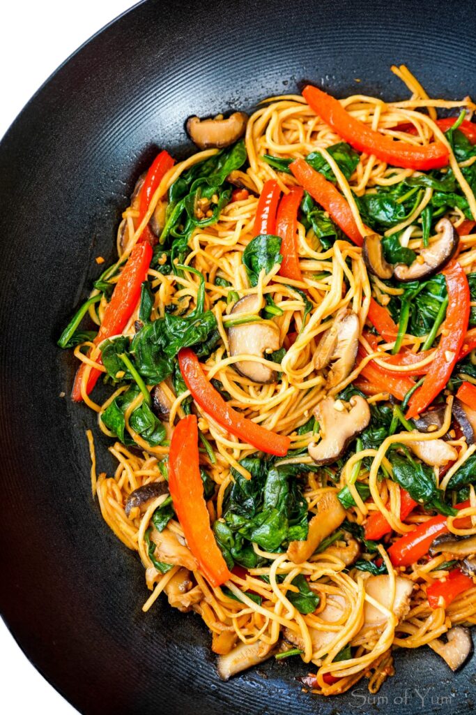 An overhead view of a colorful lo mein dish made using fresh vegetables and hearts of palm noodles, served on a large black plate.