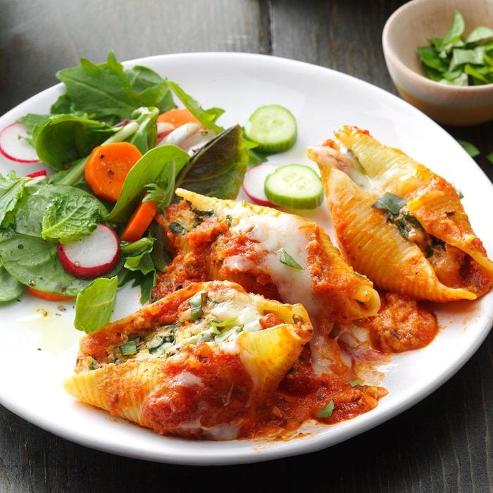 Three large stuffed pasta shells are filled with a cheesy spinach mixture and baked in a hearty tomato sauce. The low-carb, diabetic-friendly stuffed shells are served on a white plate with a fresh side salad.