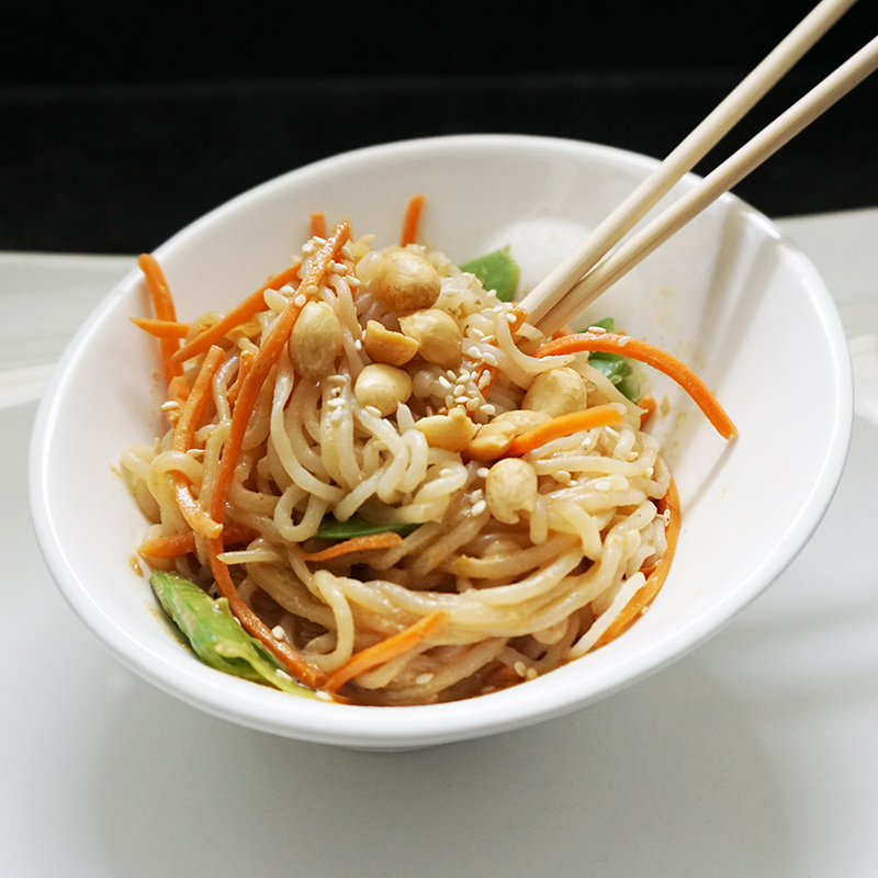 Flavorful peanut shirataki noodles and shredded colorful vegetables rest in a plunging white bowl. Chopsticks rest in the savory low-carb noodles, inviting diners to enjoy this diabetic-friendly dish. 