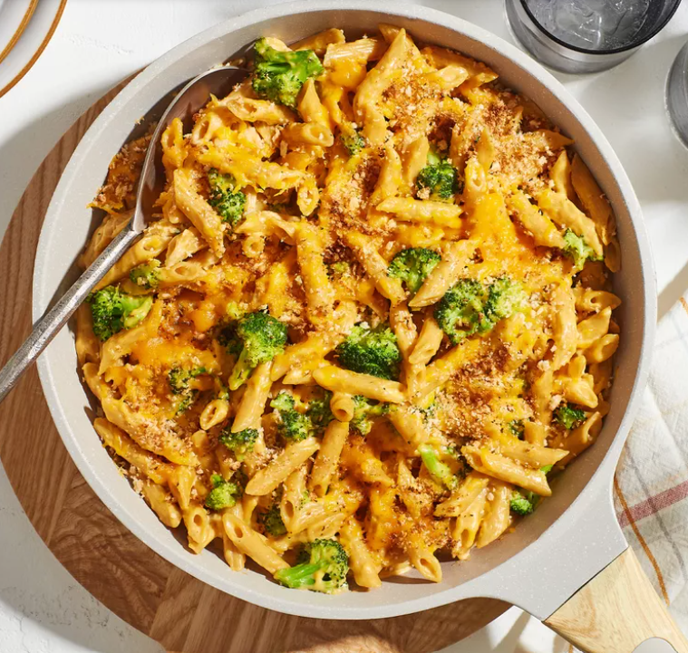 A skillet full of whole wheat penne pasta coated in a creamy cheese sauce and mixed with fresh green broccoli.